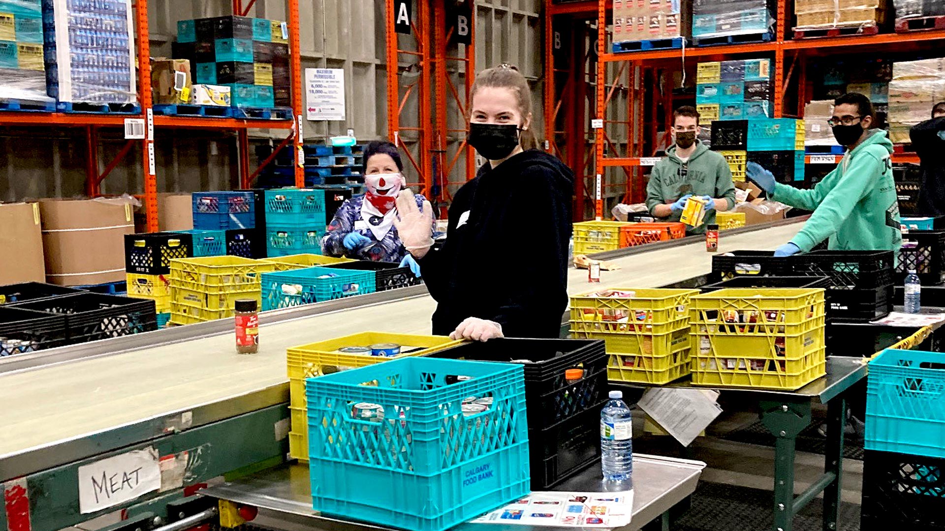A woman is standing at a sorting line for non-perishable food items waving!